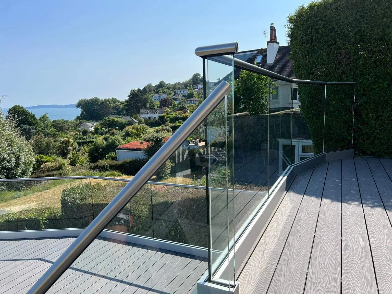 Grey composite deck with a frameless glass balustrade and steel handrail looking out to the coast
