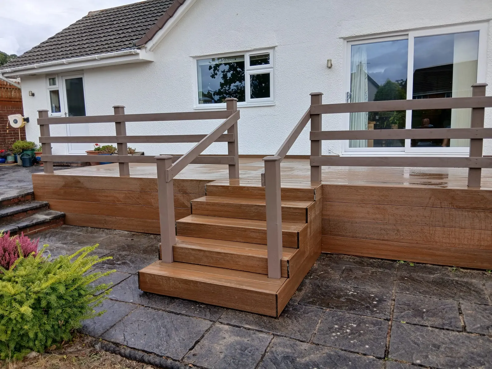 Raised wood-effect composite deck with wide steps and a taupe composite balustrade outside a bungalow