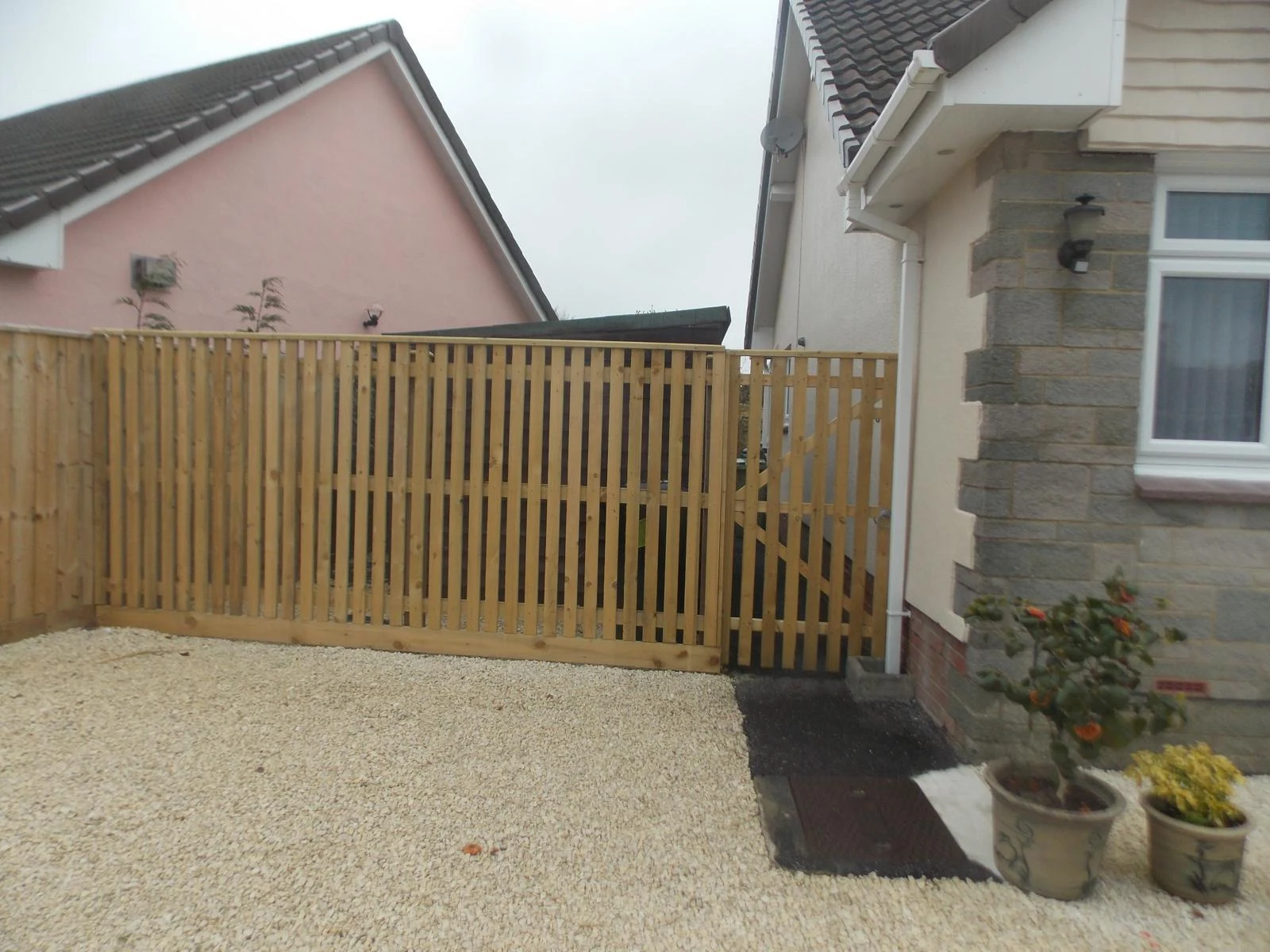 Spaced vertical board timber fence and matching side gate enclosing a gravel drive