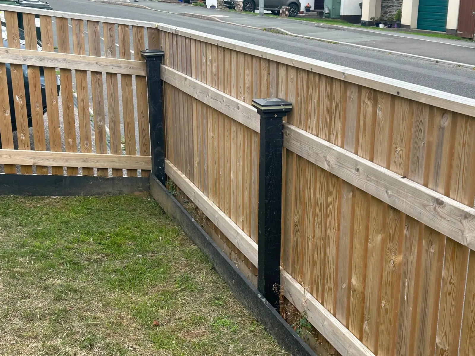 Spaced board timber fence fixed to black composite posts and gravel boards along a lawn