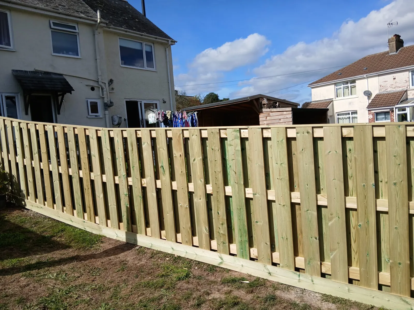 Green pressure-treated hit and miss timber fence on a gravel board along a rear garden