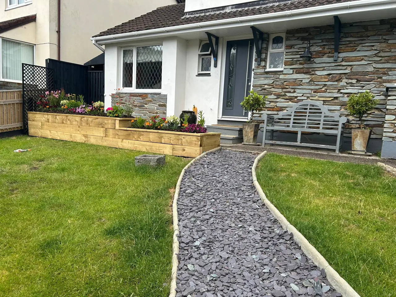 Timber sleeper raised beds along a house front, with a curved slate chipping path between two lawns