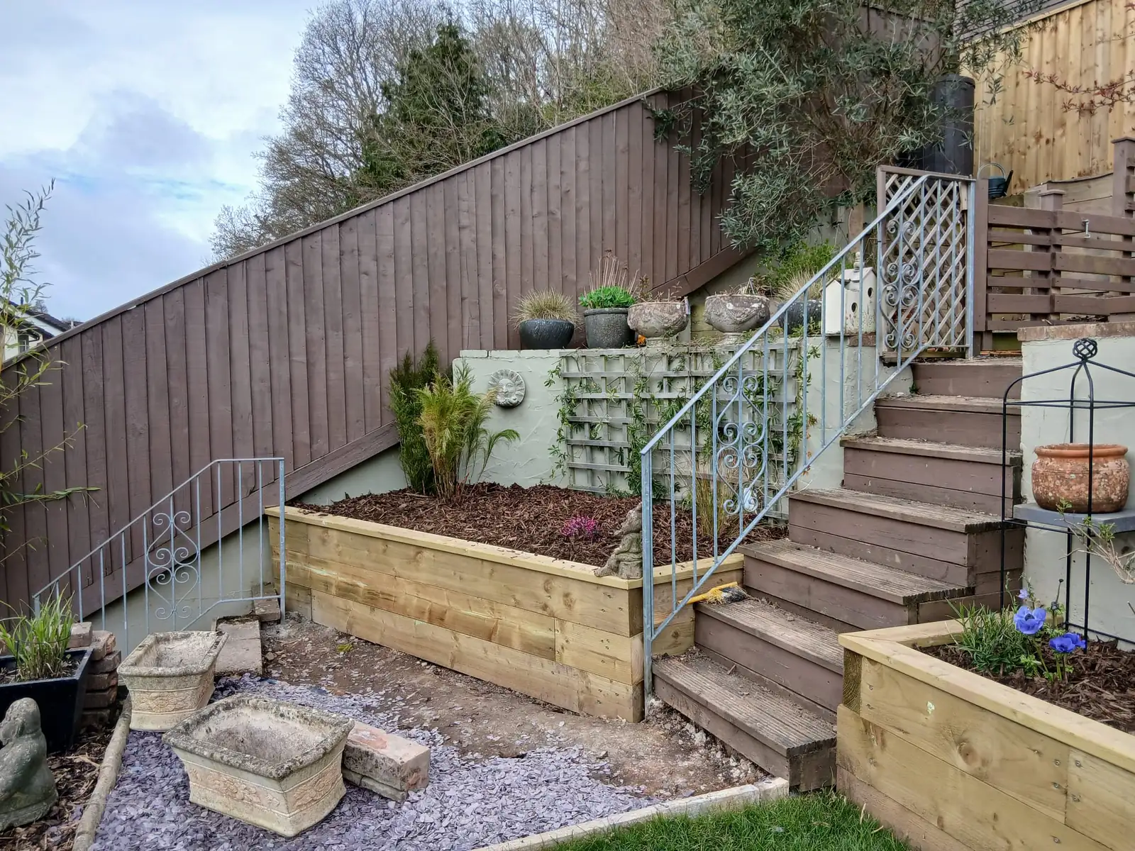 Tiered pressure-treated sleeper raised beds beside a brown painted closeboard fence and steps